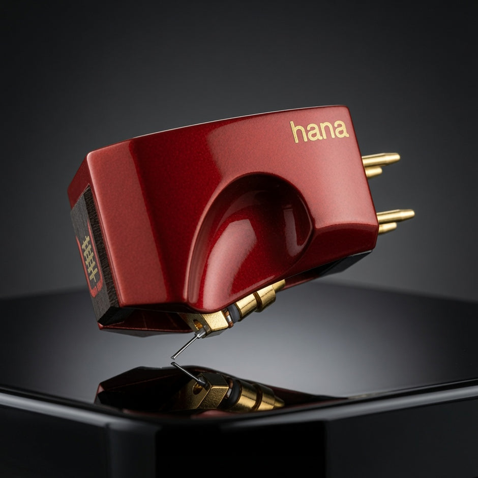 A glossy red Hana turntable cartridge shown floating above a reflective black surface against a dark studio background. The cartridge has gold-plated metal post connectors and the brand name 'hana' printed in gold on the side.